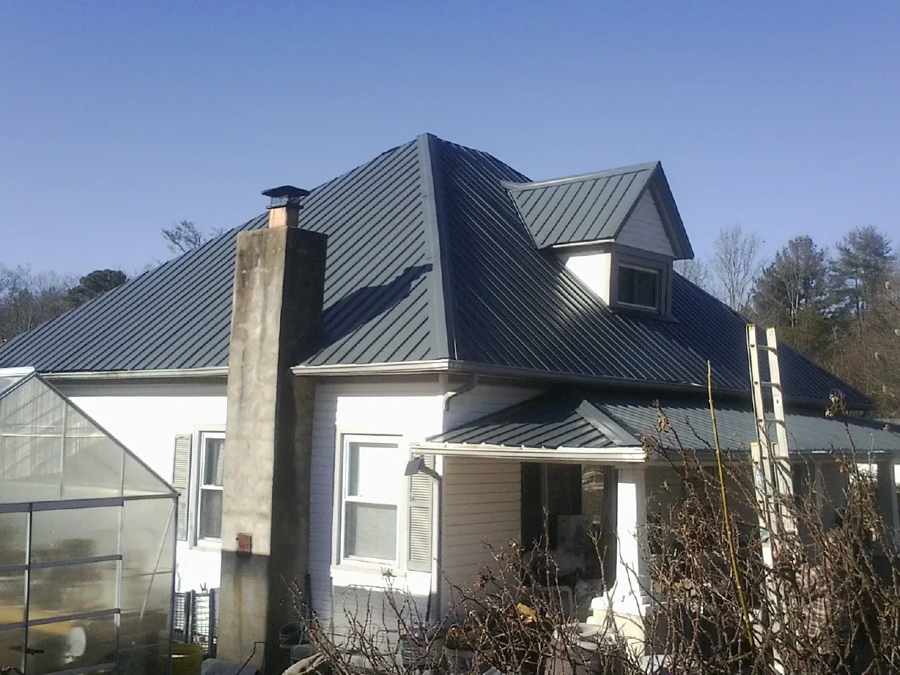 Dark blue standing seam metal roof on a white farmhouse with dormer — Slate & Tile Roof Repair by Roofing Brothers in Sargent