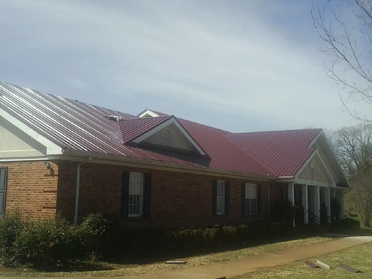 Red metal roof with gabled entries on a long brick building, from a Hail Damage Roof Repair job in Sargent