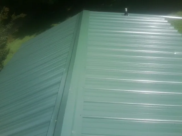 New green metal panels meeting at the ridge of a roof — Flat Roof Repair work by our crew in Sargent