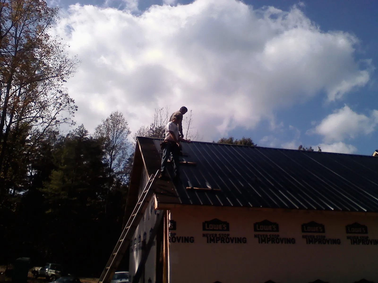 Roofer fastening dark metal panels high against a cloudy sky, from a Roof Inspection job in Sargent