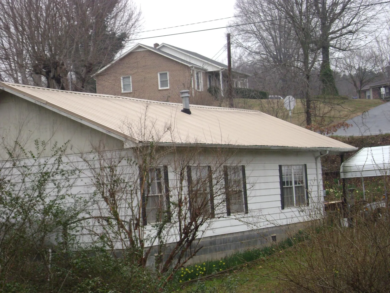 Tan metal roof on a white sided house set into a hillside — Commercial Roofing by Roofing Brothers in Sargent