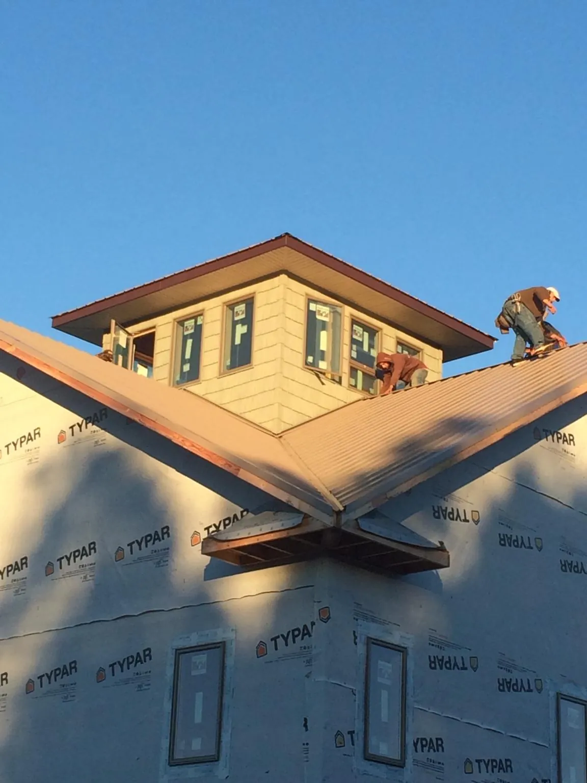 Roofers working around a rooftop cupola on a new metal roof at sunset — Roof Waterproofing in Sargent by Roofing Brothers